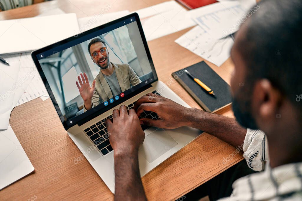 Rear view of african american videoconferencing employee with colleague at online briefing, male worker holding web conference with colleague on modern laptop at home