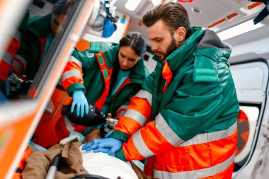 İki sağlık görevlisi ambulansta sedyede yatan bir yaşlıyı göğüs masajı yaparak ve solunum cihazına bağlanarak hayata döndürüyor..