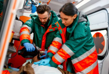 İki sağlık görevlisi ambulansta sedyede yatan bir yaşlıyı göğüs masajı yaparak ve solunum cihazına bağlanarak hayata döndürüyor..