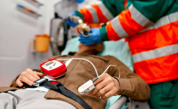 Мужчина-парамедик в форме надевает вентилятор с кислородом, чтобы помочь пожилому пациенту лежать на каталке с пульсометром в современной скорой помощи..