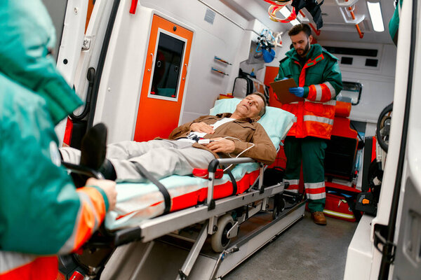 Paramedics take out a gurney with an elderly patient from a modern ambulance for further medical care at the clinic.