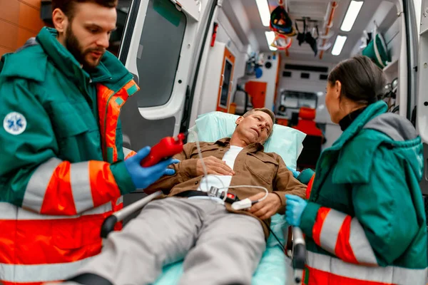 Sağlık görevlileri kandaki oksijen seviyesini kontrol ediyor ve klinikteki tıbbi bakım için modern ambulanstan yaşlı hastanın sedyesini getiriyorlar..