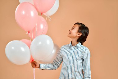 Beyaz, çizgili tişörtlü, şeftali arkaplanında izole edilmiş helyum dolu balonlar tutan beyaz bir çocuk. Sevgililer Günü 'nde..