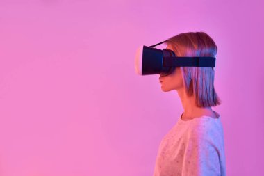 Sıradan giyinen çekici bir kadın sanal gerçeklik gözlüğü kullanıyor, yan görüş ise neon pembe arka planda izole edilmiş. VR kulaklık. Gelecekteki teknolojiler.