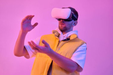 Sıradan kıyafetler giyen, sanal gerçeklik gözlüğü takan, avuçlarında neon pembe arka planda izole edilmiş bir şey tutan çekici genç bir adam. Gelecekteki teknolojiler.