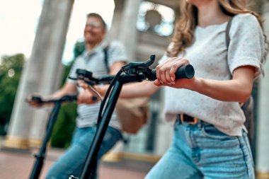 Çekici bir kız ve elektrikli scooterlı çekici bir adamın görüntüsü. Kampüsün yakınında scooter kullanan birkaç öğrenci..