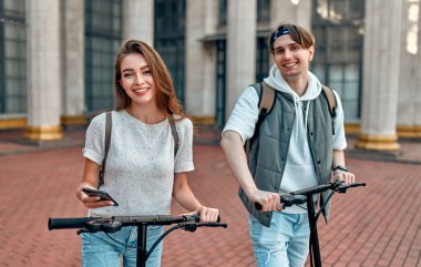 Çekici bir kız ve elektrikli scooter kullanan akıllı telefonlu çekici bir adam. Kampüsün yakınında scooter kullanan birkaç öğrenci..