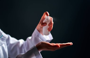 Kadın doktor eline antiseptik püskürtüyor. Koyu gri arka planda izole edilmiş. Coronavirüs salgını konsepti.