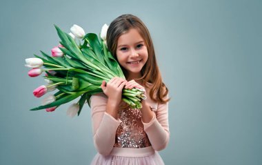 Pembe elbiseli sevimli küçük kız gri arka planda bir buket lale çiçeği tutuyor..