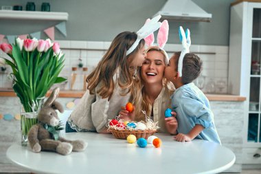 Mutlu Paskalyalar! Anne, oğul ve kız Paskalya yumurtaları için avlanmaya başlar. Çocuklar güzel annelerini yanağından öperler. Paskalya günü tavşan kulağı takan şirin bir kız ve erkek..