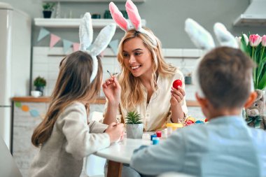 Küçük tatlı bir kız ve çocukla çekici genç bir kadın Paskalya kutlaması için hazırlanıyor. Tavşan kulağı takan mutlu aile Paskalya 'dan önce yumurta boyarken birlikte vakit geçiriyorlar..