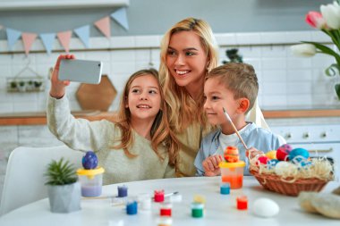 Mutlu Paskalyalar! Sevimli anne ve çocukları, tatlı oğlan ve kız, yumurta boyarken selfie çekiyorlar. Mutlu aile Paskalya için hazırlanıyor..
