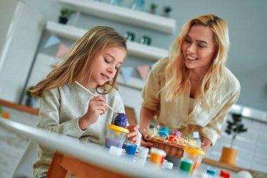 Güzel annesiyle birlikte büyüleyici bir kız Paskalya için hazırlanıyor ve mutfakta yumurta boyuyor. Anne ve kızı mutfakta eğleniyorlar..