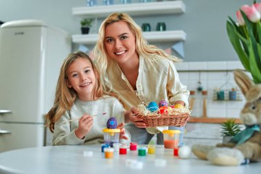 Güzel annesiyle birlikte büyüleyici bir kız Paskalya için hazırlanıyor ve mutfakta yumurta boyuyor. Anne ve kızı mutfakta eğleniyorlar..