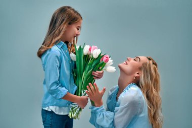 Anneler Günün kutlu olsun! Sevimli sevimli kız, güzel annesine gri arka planda izole edilmiş bir buket lale çiçeği verir..