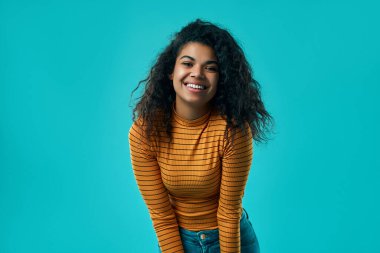 Turuncu balıkçı yaka yakalı, şık kıvırcık saçlı güzel Afrikalı Amerikalı kadın portresi parlak mavi arka planda izole edilmiş..