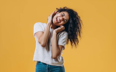 Muhteşem Afro-Amerikan kadın kulaklıkla müzik dinliyor ve sarı arka planda imza atıyor. Tişörtlü ve kulaklıklı hoş bir kız gözleri kapalı dans ediyor..