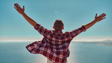 Ekose gömlekli genç bir adam denizin arka planında ellerini kaldırdı. Özgürlüğü ve zaferi simgeliyordu..