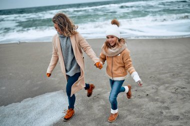 Paltolu güzel genç anne kışın kumsalda tatlı kızıyla eğleniyor..