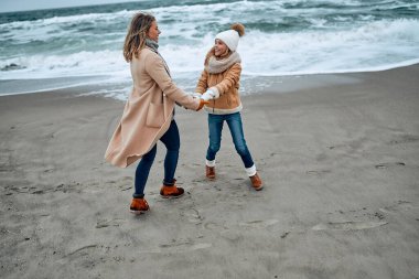 Paltolu güzel genç anne kışın kumsalda tatlı kızıyla eğleniyor..