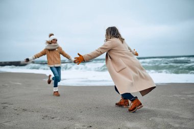 Paltolu güzel genç anne kışın kumsalda tatlı kızıyla eğleniyor..