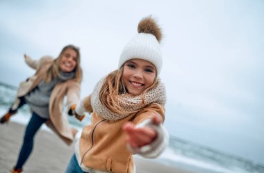Paltolu güzel genç anne kışın kumsalda tatlı kızıyla eğleniyor..