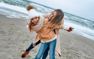 Paltolu güzel genç anne kışın kumsalda tatlı kızıyla eğleniyor..