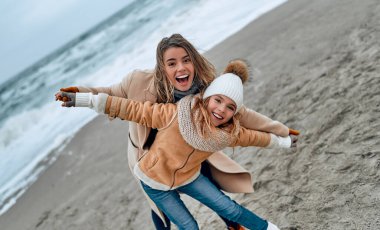 Paltolu güzel genç anne kışın kumsalda tatlı kızıyla eğleniyor..