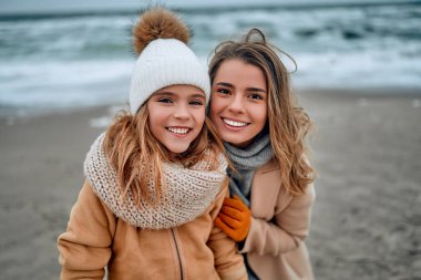 Paltolu güzel genç anne kışın kumsalda tatlı kızıyla eğleniyor..