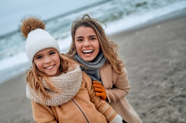 Paltolu güzel genç anne kışın kumsalda tatlı kızıyla eğleniyor..