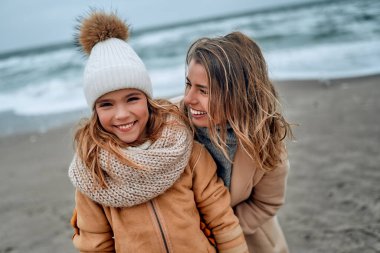 Paltolu güzel genç anne kışın kumsalda tatlı kızıyla eğleniyor..