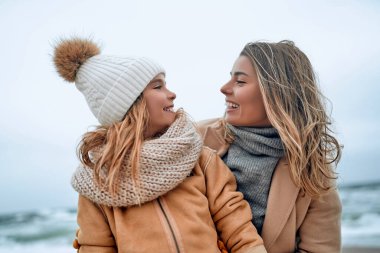 Paltolu güzel genç anne kışın kumsalda tatlı kızıyla eğleniyor..