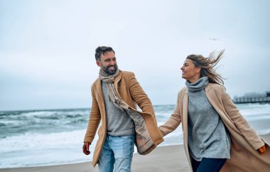 Birbirlerine aşık güzel evli çiftler soğuk mevsimde deniz kıyısında palto giyip eğleniyorlar..