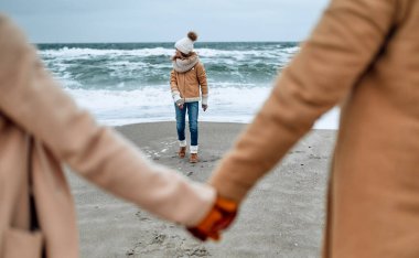 Örgü şapkalı ve eldivenli çekici bir kız ailesi ile birlikte soğuk mevsimde deniz kıyısında dinleniyor..