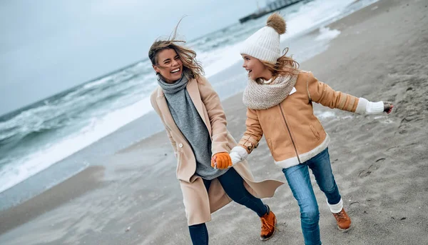 Paltolu güzel genç anne kışın kumsalda tatlı kızıyla eğleniyor..