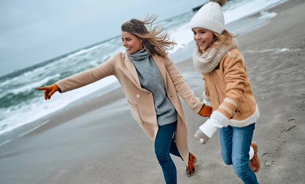 Paltolu güzel genç anne kışın kumsalda tatlı kızıyla eğleniyor..