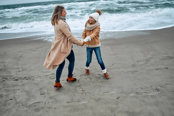 Paltolu güzel genç anne kışın kumsalda tatlı kızıyla eğleniyor..