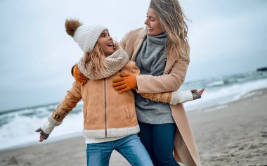 Paltolu güzel genç anne kışın kumsalda tatlı kızıyla eğleniyor..