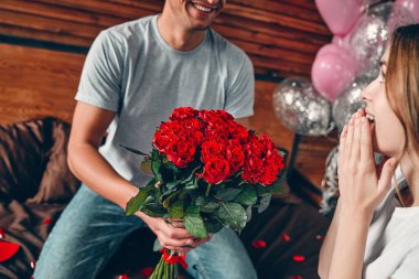 Sevgililer Günü 'nü kutluyoruz. Bir erkek bir kadına kırmızı güller verir. Bir çift kalp şeklinde konfetiyle yatakta oturuyor..