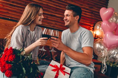 Genç çift yatak odasında şarap kadehleri, hediye ve kırmızı güllerle. Sevgililer Günü. Yıldönümü. Doğum günü.