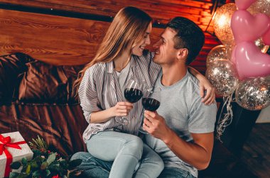 Genç çift yatak odasında şarap kadehleri, hediye ve kırmızı güllerle. Sevgililer Günü. Yıldönümü. Doğum günü.