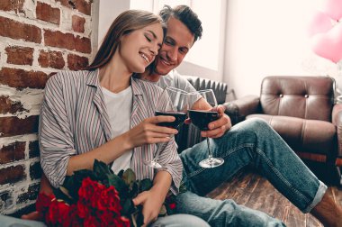 Yerde oturan genç çift ellerinde şarap ve kırmızı güllerle. Sevgililer Günü. Yıldönümü. Doğum günü.