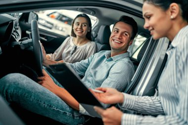 Genç bayan danışman ve çift alıcılar araba fuarında yeni araba imzalama kontratında oturuyorlar. Araba kiralama kavramı.