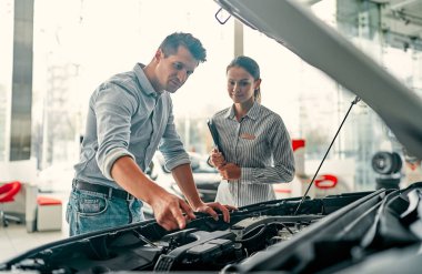 İlk arabamı alıyorum. Galeride duran genç araba satıcısı kaputun altındaki arabanın özelliklerini yakışıklı adama anlatıyor..