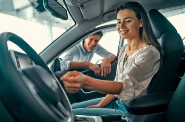 Genç ve güzel bir çift yeni bir araba seçiyor. Bir kadın arabada oturur, ve bir erkek kapıyı gözetler. Satın alma ve araba kiralama.