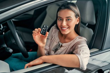 Genç mutlu kadın yeni arabanın anahtarını gösteriyor. Arabayı alan kadın..