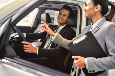 Araba galerisindeki müşteriyle çalışırken profesyonel satış elemanı. Takım elbiseli başarılı genç işadamı yeni bir araba seçiyor..