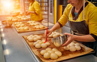 Fırıncılar daha fazla pişirmek için çörekleri ayçiçeği yağıyla yağlıyorlar. Otomatik fırın ürünleri üretimi. Ekmek fabrikası.