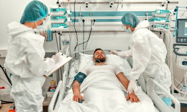 Koruyucu giysili, gözlüklü ve maskeli doktorlar yoğun bakım ünitesinde Coronavirus hastalığı olan bir hastanın durumunu izliyorlar. Modern bir klinikte salgın sırasında tedavi.