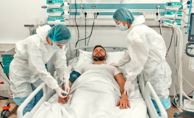 Koruyucu giysili, gözlüklü ve maskeli doktorlar yoğun bakım ünitesinde Coronavirus hastalığı olan bir hastanın durumunu izliyorlar. Modern bir klinikte salgın sırasında tedavi.